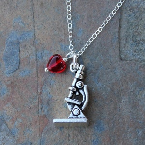 May include: A silver necklace with a microscope charm and a red glass heart charm.