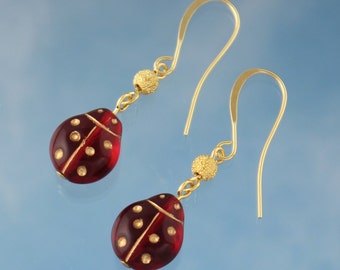 May include: A pair of gold dangle earrings with red ladybug charms. The ladybugs have gold dots and a gold line down the center.
