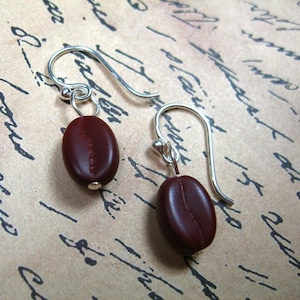 Peut inclure: Une paire de boucles d'oreilles pendantes en argent avec des breloques en forme de grains de café bruns.