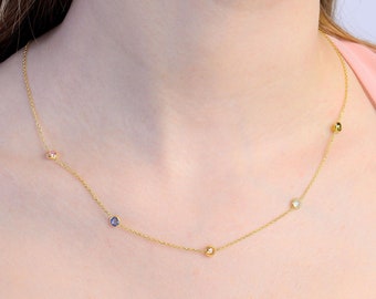 Op de afbeelding: Een fijne gouden ketting met een delicate ketting, bezet met kleine, kleurrijke edelstenen. De ketting heeft roze, blauwe, gele en heldere stenen. De ketting wordt om de hals gedragen en toont de edelstenen.