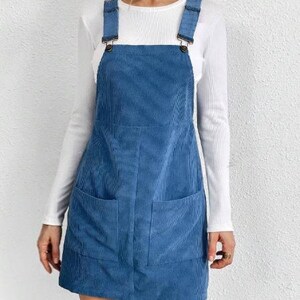 May include: A blue corduroy pinafore dress with two pockets. The dress has adjustable straps with metal buckles.