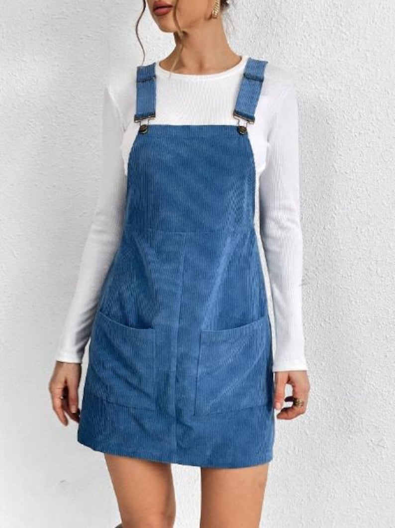 May include: A blue corduroy pinafore dress with two pockets. The dress has adjustable straps with metal buckles.