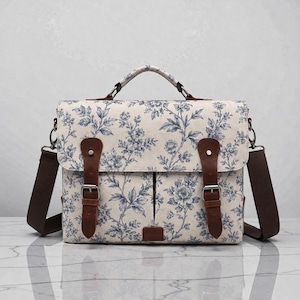 Pu&ograve; includere: Una borsa a tracolla in tessuto color crema con motivo floreale blu. Include un manico superiore, una tracolla marrone rimovibile e due cinghie in similpelle marrone con fibbie in metallo color argento sulla patta anteriore.