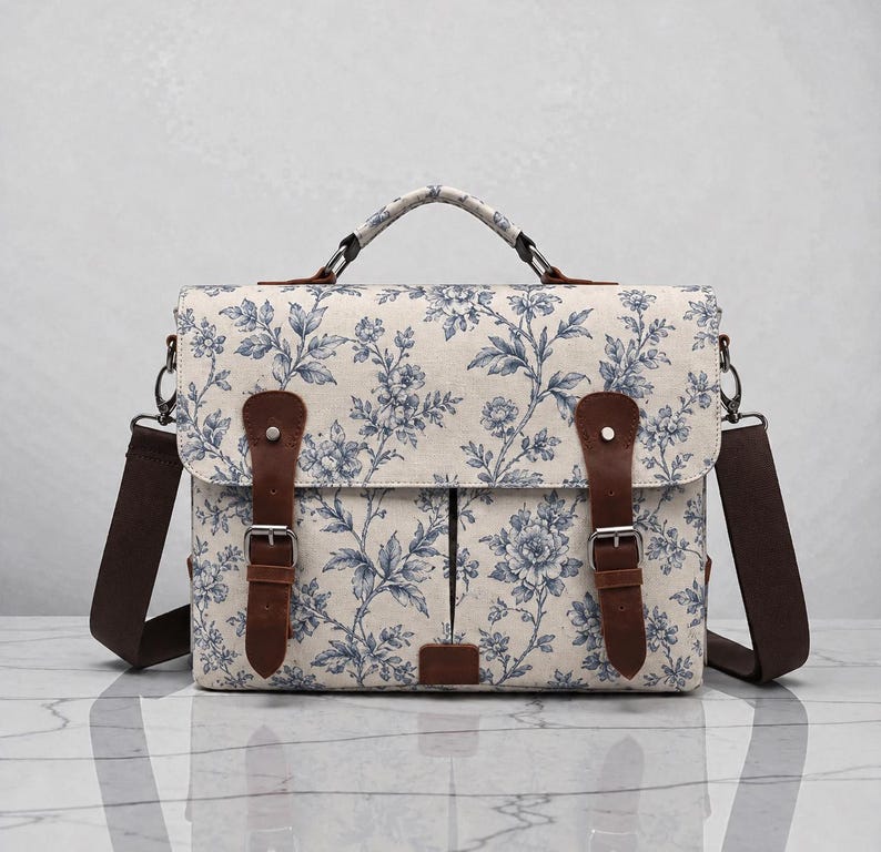 Pu&ograve; includere: Una borsa a tracolla in tessuto color crema con motivo floreale blu. Include un manico superiore, una tracolla marrone rimovibile e due cinghie in similpelle marrone con fibbie in metallo color argento sulla patta anteriore.