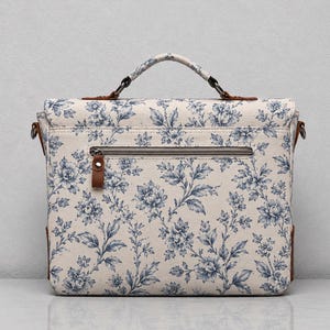 Pu&ograve; includere: Una borsa a cartella rettangolare con base color crema e motivo floreale blu. La borsa presenta un manico superiore, una tasca orizzontale con cerniera sul davanti e dettagli in similpelle marrone sugli attacchi del manico e sulla zip.