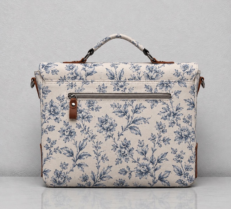 Pu&ograve; includere: Una borsa a cartella rettangolare con base color crema e motivo floreale blu. La borsa presenta un manico superiore, una tasca orizzontale con cerniera sul davanti e dettagli in similpelle marrone sugli attacchi del manico e sulla zip.