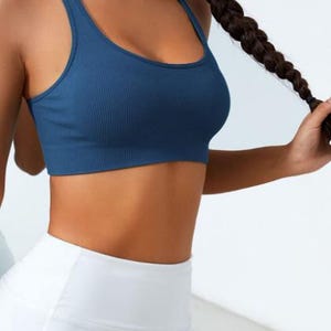 May include: A blue ribbed sports bra with a scoop neck and racerback design. The bra is paired with white leggings. The image shows a close-up of the top and bottom, highlighting the athletic wear.