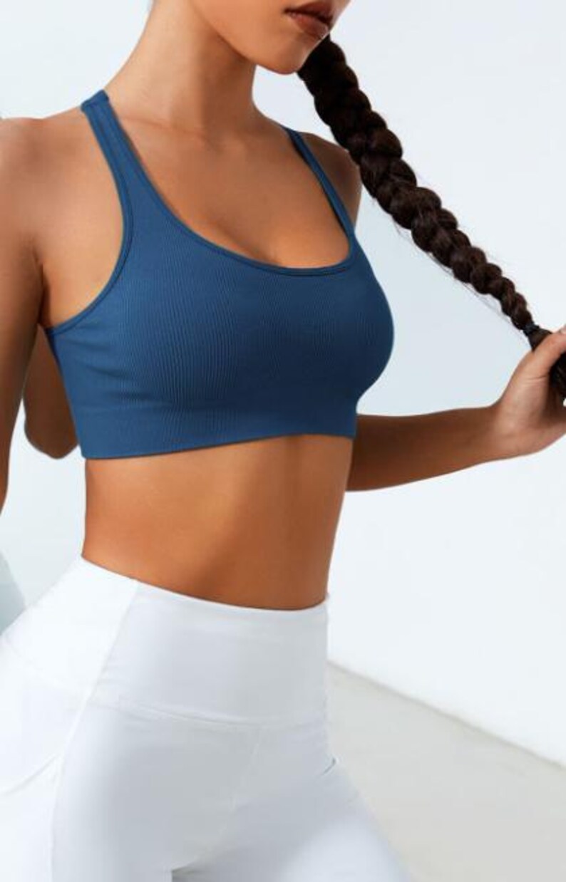 May include: A blue ribbed sports bra with a scoop neck and racerback design. The bra is paired with white leggings. The image shows a close-up of the top and bottom, highlighting the athletic wear.