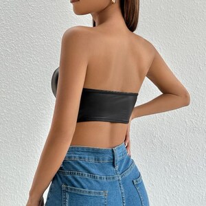 Peut inclure: Un top court noir sans bretelles en similicuir. Le haut a une silhouette ajust&eacute;e et un d&eacute;collet&eacute; droit. Le mannequin porte le haut avec un jean bleu.