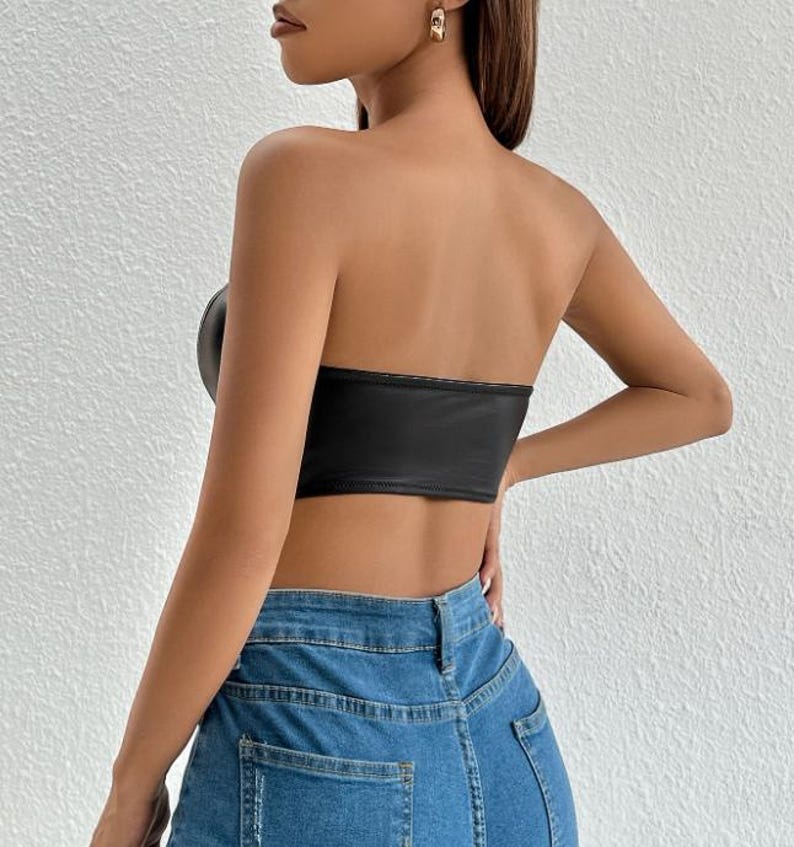 Peut inclure: Un top court noir sans bretelles en similicuir. Le haut a une silhouette ajust&eacute;e et un d&eacute;collet&eacute; droit. Le mannequin porte le haut avec un jean bleu.