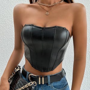 Peut inclure: Un haut de corset sans bretelles en similicuir noir avec un ourlet pointu et des d&eacute;tails de couture. Le haut est port&eacute; avec une ceinture noire &agrave; strass et un jean bleu.