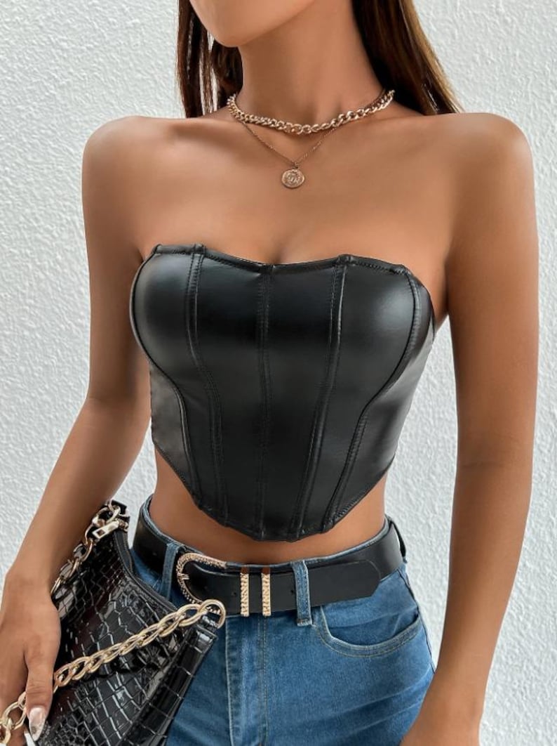 Peut inclure: Un haut de corset sans bretelles en similicuir noir avec un ourlet pointu et des d&eacute;tails de couture. Le haut est port&eacute; avec une ceinture noire &agrave; strass et un jean bleu.