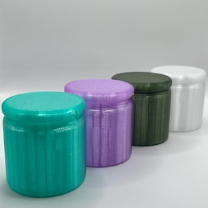 Peut inclure: Quatre petits contenants cylindriques avec des surfaces texturées. Les contenants sont dans des tons de turquoise, lavande, vert foncé et blanc.