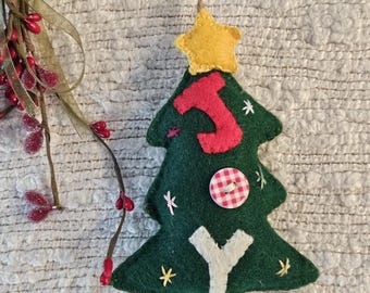 Può includere: Un ornamento per l'albero di Natale fatto a mano. L'albero di feltro verde è adornato con una lettera "J" rossa, una lettera "Y" bianca, un bottone a scacchi rosso e bianco e piccoli accenti di stelle gialle. Una stella gialla in cima all'albero.