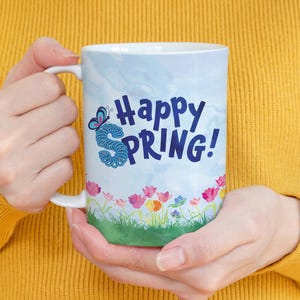 May include: White ceramic mug with a blue and white watercolor background. The mug features a blue butterfly and the text "Happy Spring!" in blue lettering.