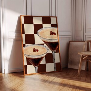 May include: Two martini glasses filled with a coffee-colored liquid and topped with a layer of cream. The glasses are on a brown and white checkered background.