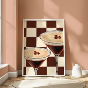 May include: Two espresso martinis with a brown and white checkered background. The drinks are topped with a layer of foam and coffee beans.