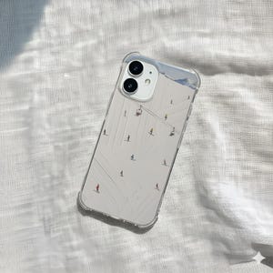 May include: Clear phone case with a winter ski resort design. The case features a white background with skiers, ski lifts, and a mountain range at the top. The case is designed to fit a smartphone with a dual-camera system.
