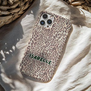 May include: A phone case with a leopard print design in shades of brown and tan. The name "ISABELLE" is printed in green letters on the case. The case has a camera cutout.