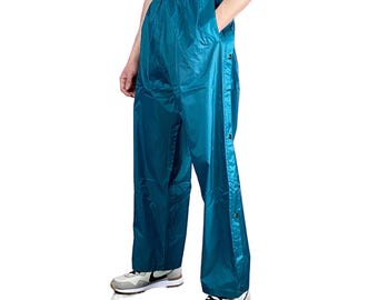 May include: Teal-colored athletic pants with snap-button closures down the sides. The pants have an elastic waistband and pockets. The person in the image is wearing gray sneakers.