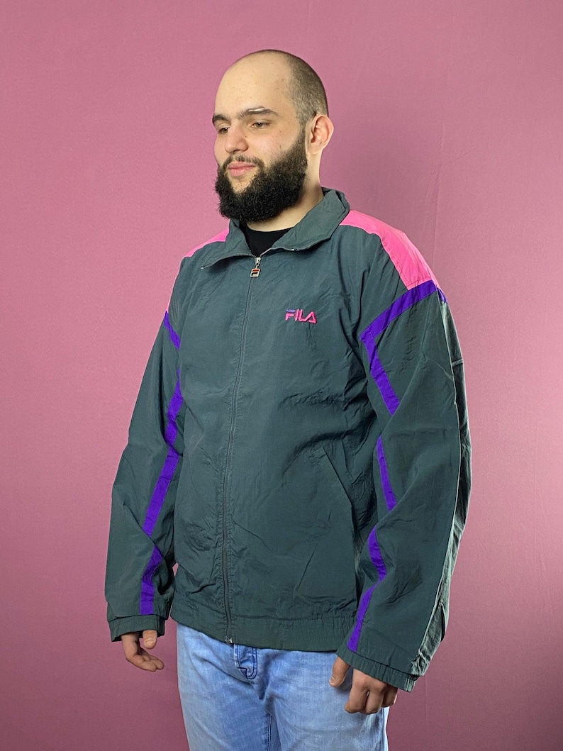 May include: A dark green jacket with purple and pink accents. The jacket has a zipper closure and a logo that says "FILA" on the left chest.
