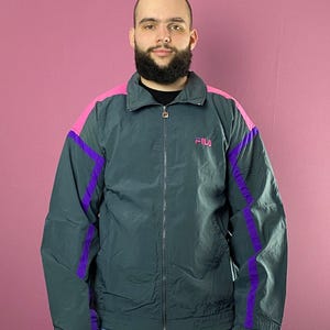May include: A dark green jacket with purple and pink accents. The jacket has a zipper closure and a logo that says "FILA" on the chest.