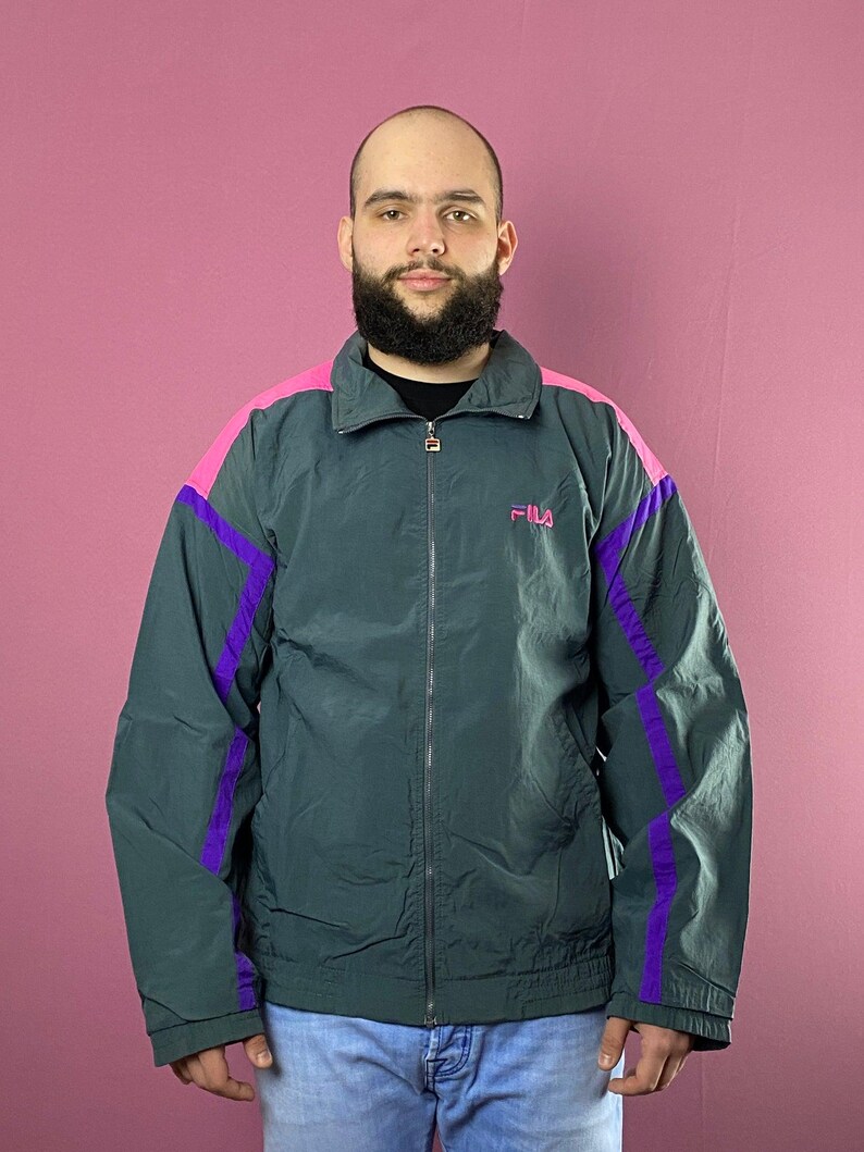 May include: A dark green jacket with purple and pink accents. The jacket has a zipper closure and a logo that says "FILA" on the chest.
