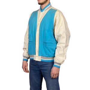 Op de afbeelding: Een blauw en wit varsity jack met een drukknoopsluiting en geribbelde manchetten en tailleband.