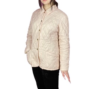 May include: A light pink quilted jacket with a button-up front and two pockets.
