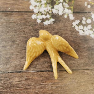 May include: A ceramic yellow swallow figurine with a textured surface. The swallow is in flight with its wings spread out.