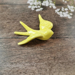 May include: A yellow ceramic bird figurine with a white speckled pattern. The bird is in flight with its wings spread out.