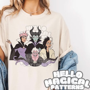 May include: A cream-coloured t-shirt with a graphic of four cartoon villains: a queen in purple, a horned figure, a woman with black and white hair, and Ursula. The text "HELLO MAGICAL PATTERNS" is also visible.