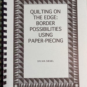 May include: A spiral-bound instructional book titled Quilting on the Edge: Border Possibilities Using Paper-Piecing by Sylvia Siegel. The cover features a black and white geometric border pattern of triangles and squares on a light gray background.