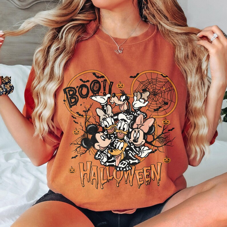 May include: Orange t-shirt with a graphic print of Mickey Mouse and friends dressed in Halloween costumes. The text "BOO! HALLOWEEN" is printed on the shirt.