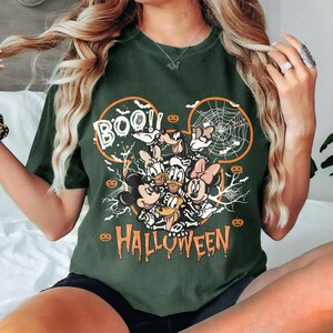 May include: A green t-shirt with a graphic of Mickey Mouse and friends dressed as skeletons for Halloween. The graphic includes the text "BOO!" and "HALLOWEEN".