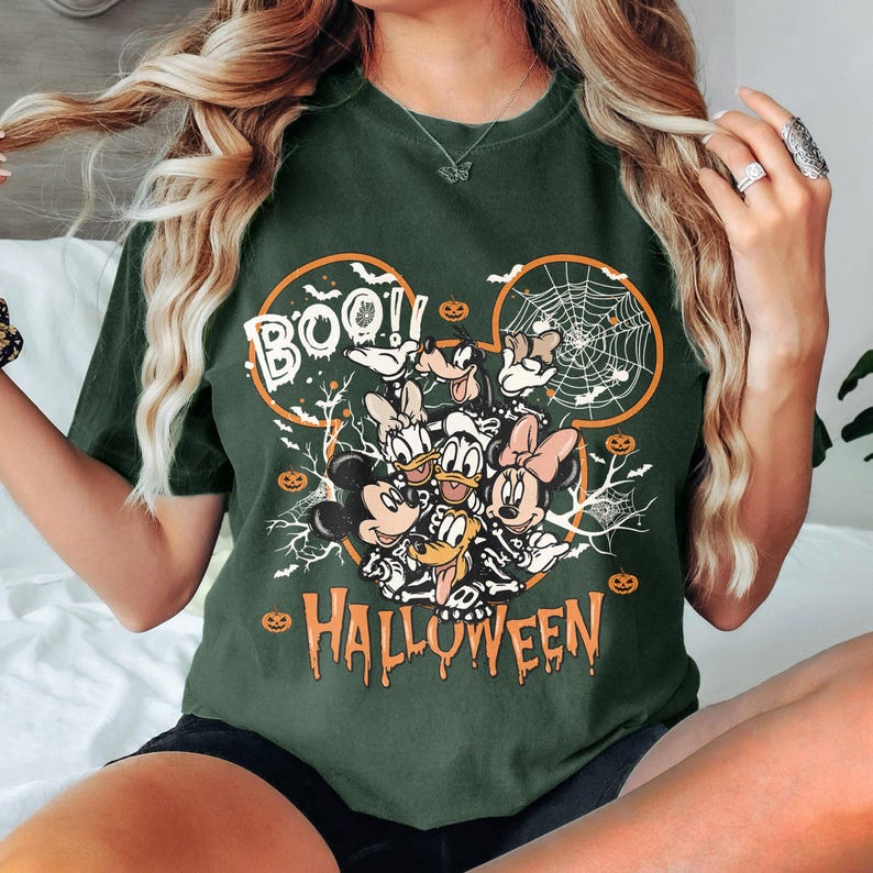 May include: A green t-shirt with a graphic of Mickey Mouse and friends dressed as skeletons for Halloween. The graphic includes the text "BOO!" and "HALLOWEEN".