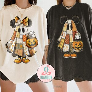 Peut inclure: Deux t-shirts amples, un crème et un charbon de bois, avec un motif sur le thème d'Halloween. Le motif représente un personnage fantôme avec des oreilles de Mickey Mouse, une tenue patchwork et une lanterne citrouille. Les t-shirts sont décontractés.
