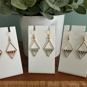 May include: Three pairs of gold triangle earrings with beaded accents. The earrings are displayed on white card stock.