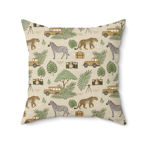 May include: Square throw pillow with a safari-themed pattern. The design features zebras, leopards, vintage cameras, safari vehicles, suitcases, and tropical foliage in shades of tan, green, and brown.