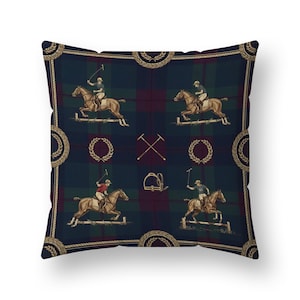 May include: Square cushion with a navy, green, and burgundy tartan pattern. The design features illustrations of polo players on horseback jumping hurdles, surrounded by gold laurel wreaths and rope trim.