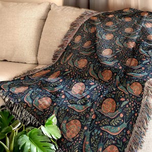 Woven blanket with a dark blue snail and floral pattern draped over a sofa.