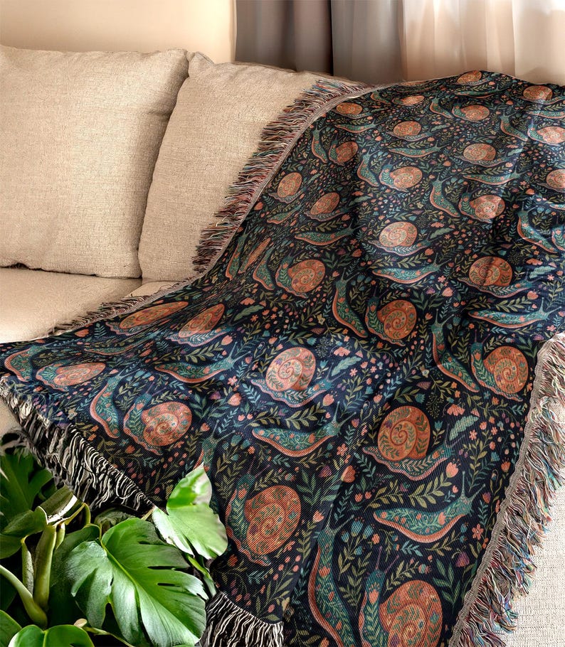 Woven blanket with a dark blue snail and floral pattern draped over a sofa.