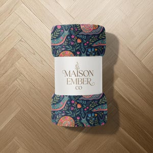 Rolled blanket with snail and floral pattern and Maison Ember Co. label.