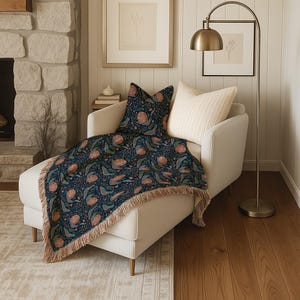 Cream chaise lounge with a dark blue throw blanket featuring a floral and bird pattern.