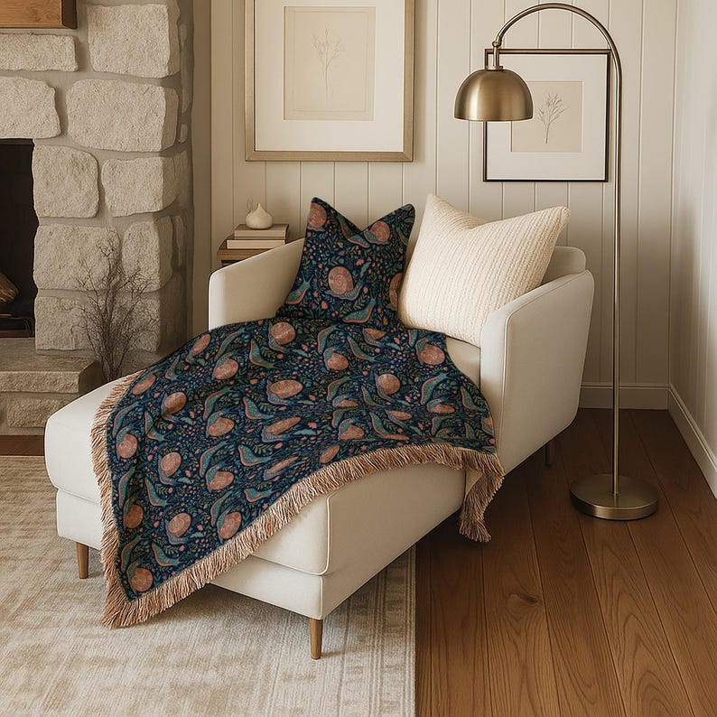 Cream chaise lounge with a dark blue throw blanket featuring a floral and bird pattern.