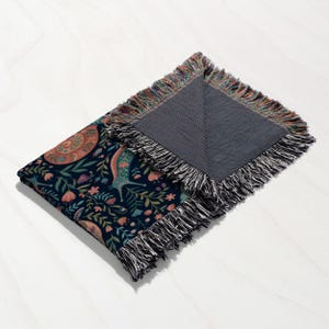 Navy blanket with intricate floral and animal pattern and fringed edges.