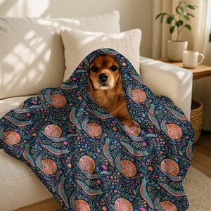 Cavalier King Charles Spaniel peeking out from under a colorful snail-patterned blanket.