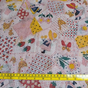 May include: A white fabric featuring a patchwork print of children in sun hats, strawberries, flowers, and yellow geometric shapes. A yellow measuring tape is placed across the bottom, showing measurements in inches and centimeters.