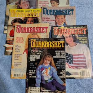 May include: A collection of seven vintage Workbasket and Home Arts magazines featuring various cover models, seasonal themes, and craft project headlines including holiday gifts, sweaters, and Americana designs with visible barcodes and issue dates.