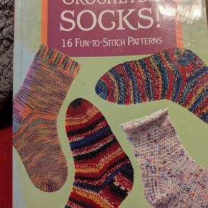 May include: A book cover titled "CROCHETED SOCKS!" with the subtitle "16 Fun-to-Stitch Patterns." The cover features four colorful crochet sock designs against a green background. The authors' names, Janet Rehfeldt and Mary Jane Wood, are at the bottom.
